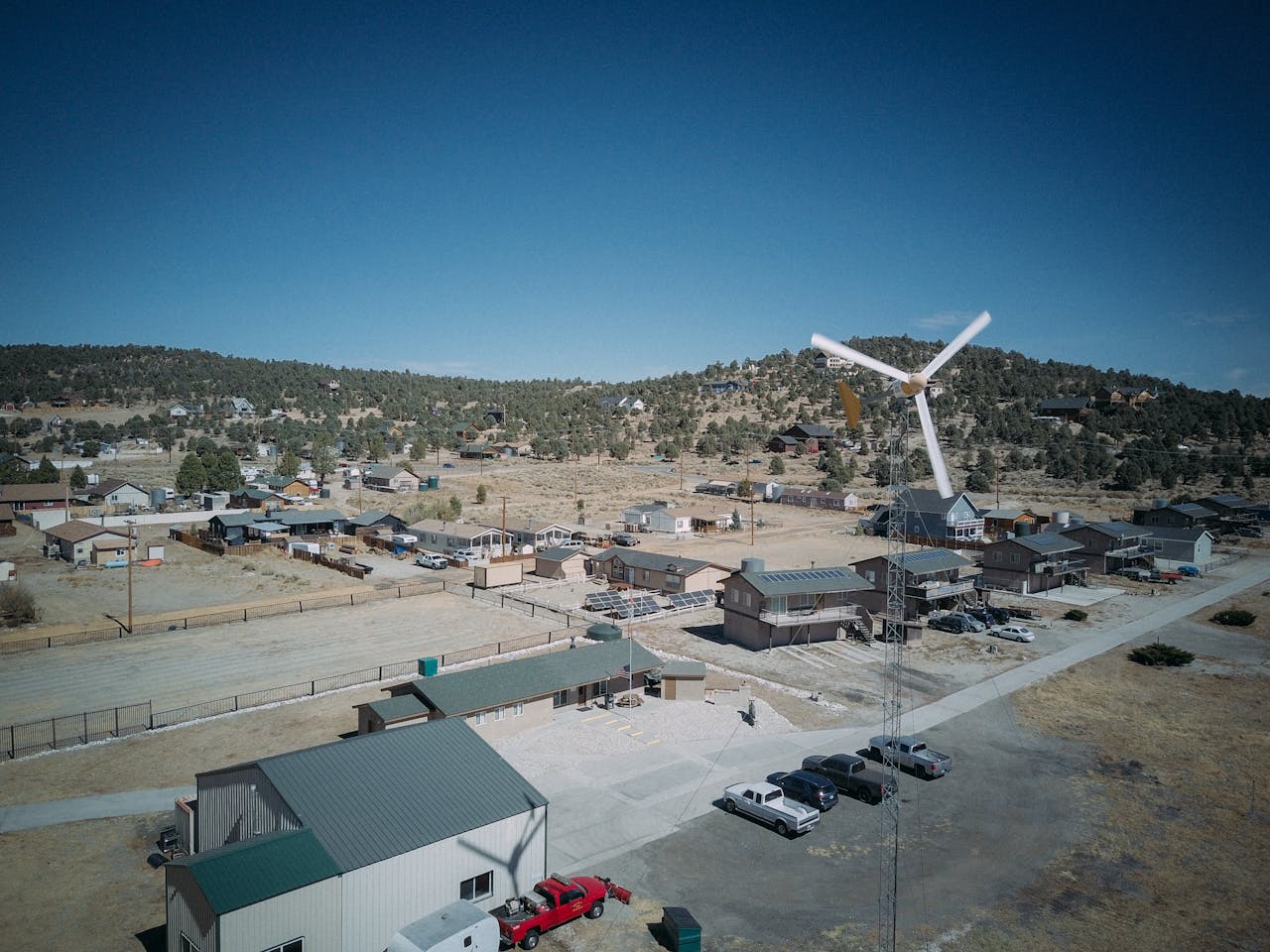 A drone captures a wind turbine and suburban area on a clear day.